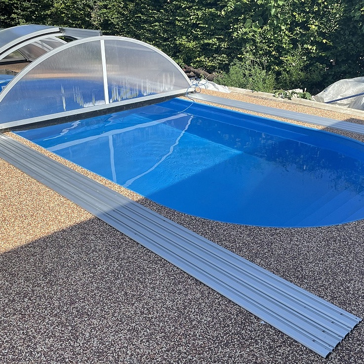 Modrý oválný bazén se schodištěm přes celou šíři a obloukovým zastřešením Praktik