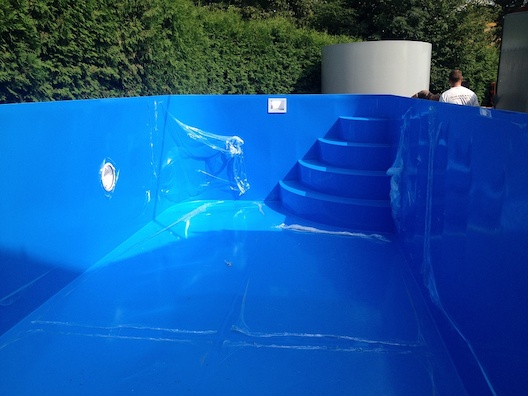 Zaoblený modrý bazén s bílými nášlapy a modrou lemovou trubkou