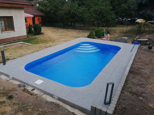 Zaoblený modrý bazén s bilými nášlapy