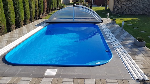 Zaoblený modrý bazén s bilými nášlapy a lemovou trubkou